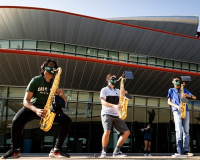 Three members of Mustang Band play the saxophone while wearing face coverings