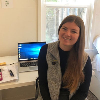 A student sits in her bedroom in front of her open laptop.