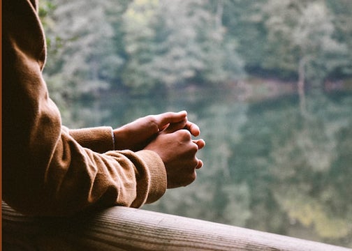 A person leans on a fense post overlooking a lake reflecting evergreen trees