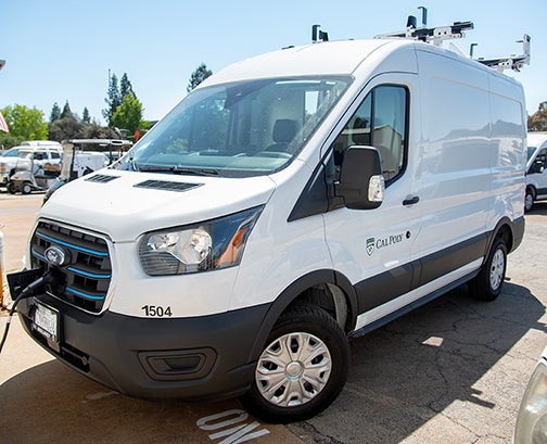 An electric van parked in a parking space at Cal Poly, plugged in to charge.