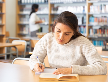 A person reads and takes notes at a desk.