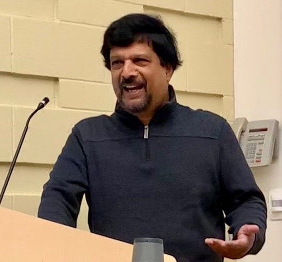 Suresh Canagarajah stands behind a podium, speaking and gesturing with his left hand.