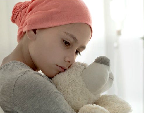 A child cancer patient with a scarf covering the head hugs a teddy bear