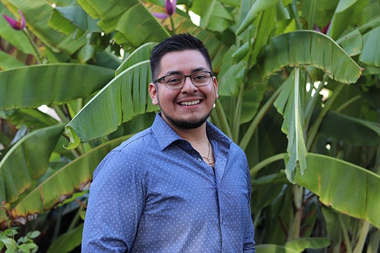 A young man in glasses and a blue button-up shirt smiles into the camera