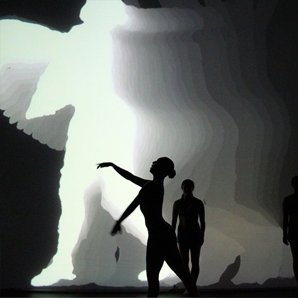 A silhouette of a female dancer facing left with her arms extended as the screen behind her mimics the same movements with a shadow reflection effect.