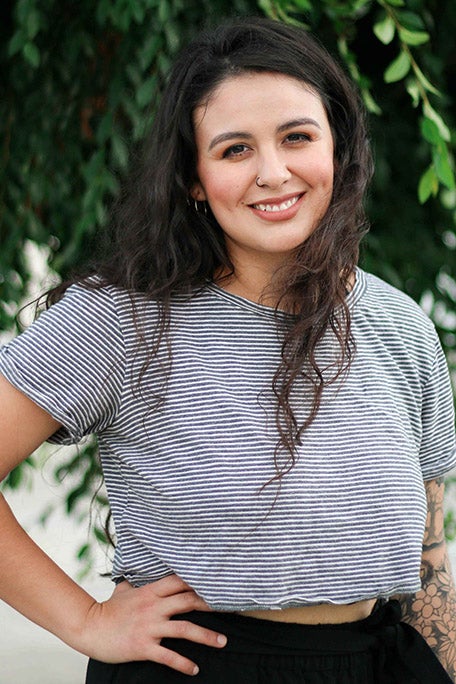 A young woman smiles in a white and black striped top with her hand on her hip