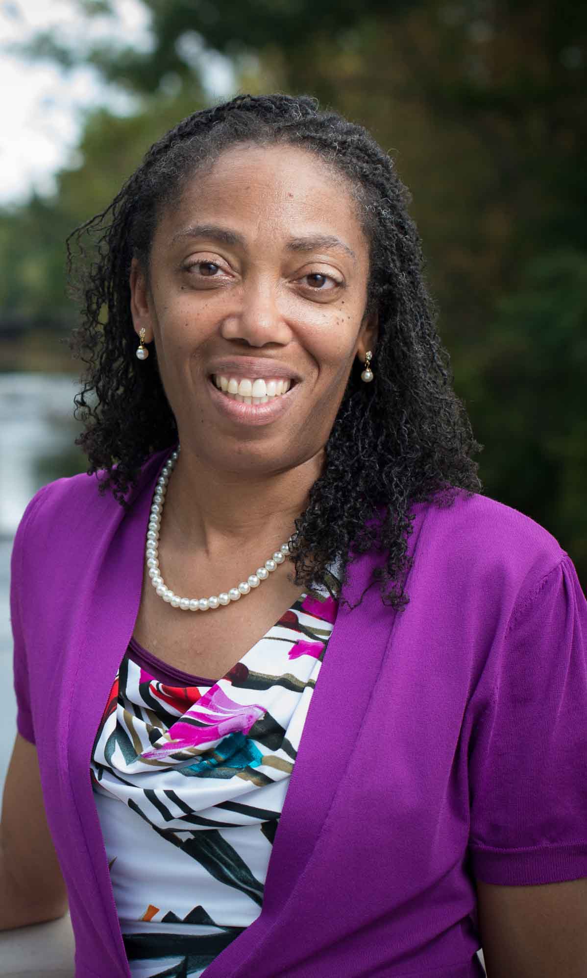 A woman in a purple jacket and a print top smiles at the camera.