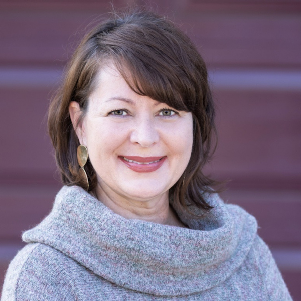 A woman with brown hair wearing a gray sweater smiles at the camera.