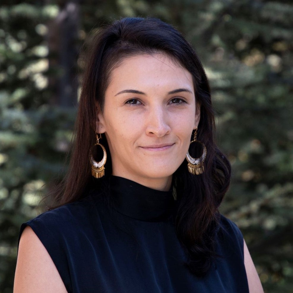 A woman in a black blouse looks at the camera for a professional headshot.