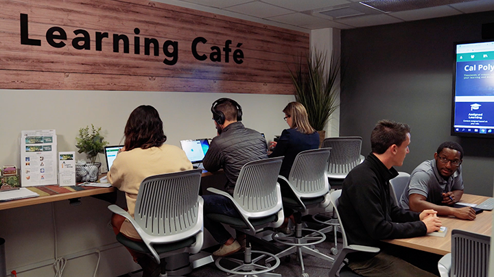 Several staff members sit inside the learning cafe in front of computers or working together at a center table.