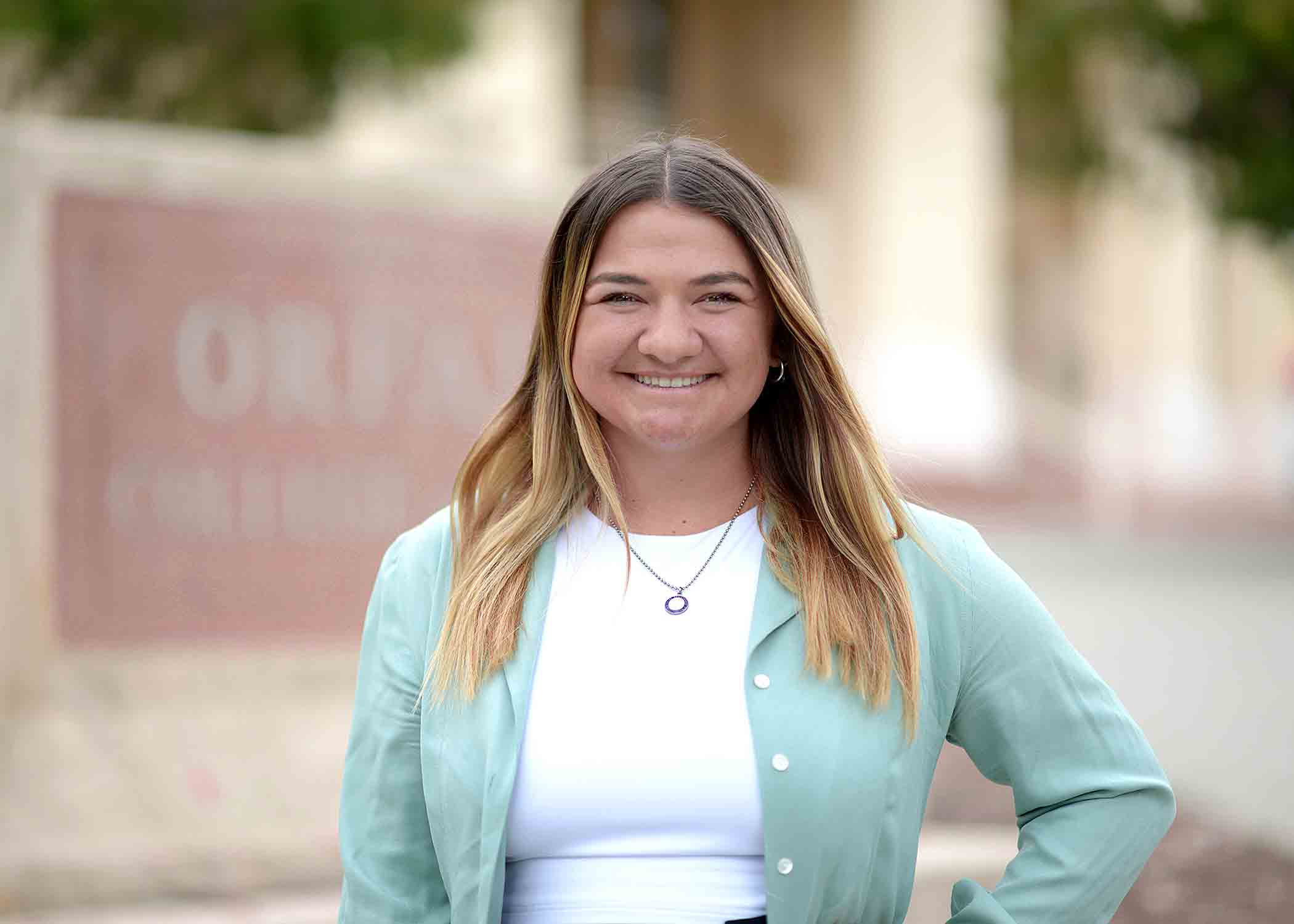 Carolyn Lidster wears a teal overshirt over a white shirt in front of the Orfalea College of Business.