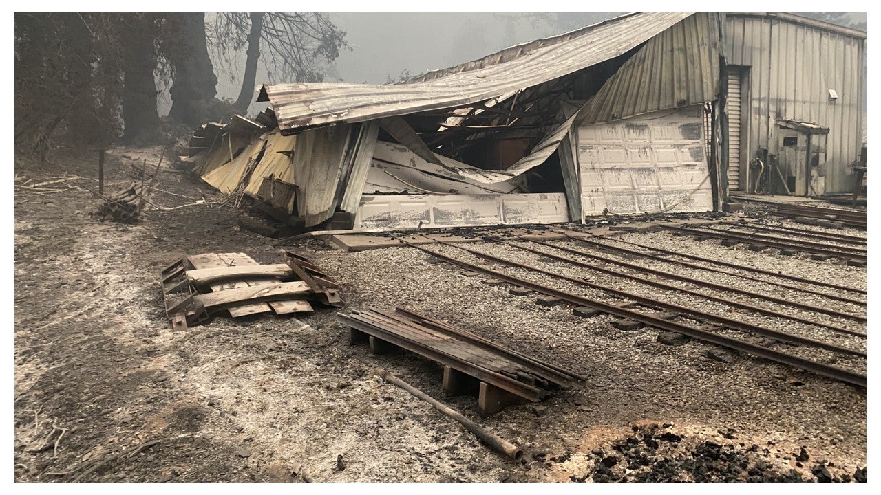 A crumpled and fire-damaged warehouse and railroad tracks