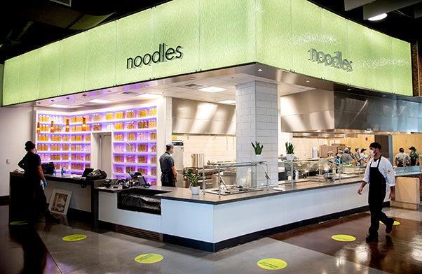 A lit-up food counter decorated with jars of pasta and topped with a sign reading "Noodles"