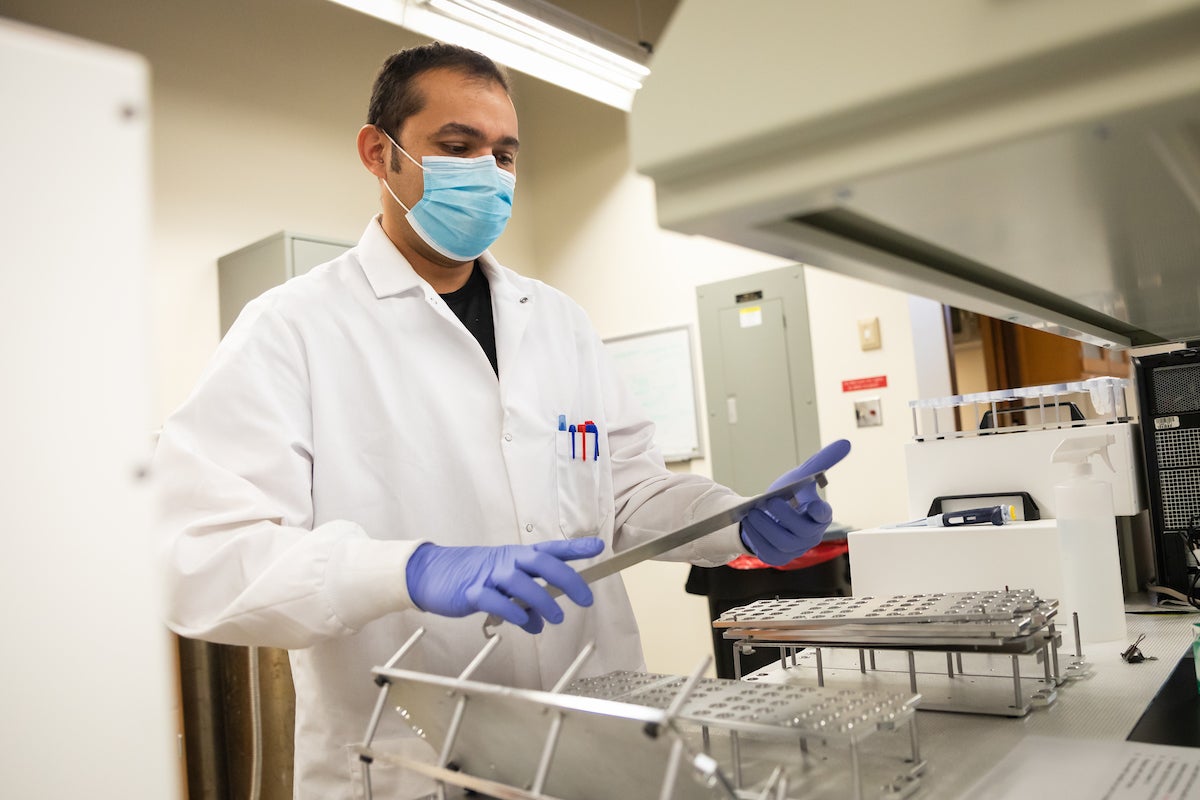 A man in a lab coat, mask and gloves handles a sample tray in a coronavirus testing lab