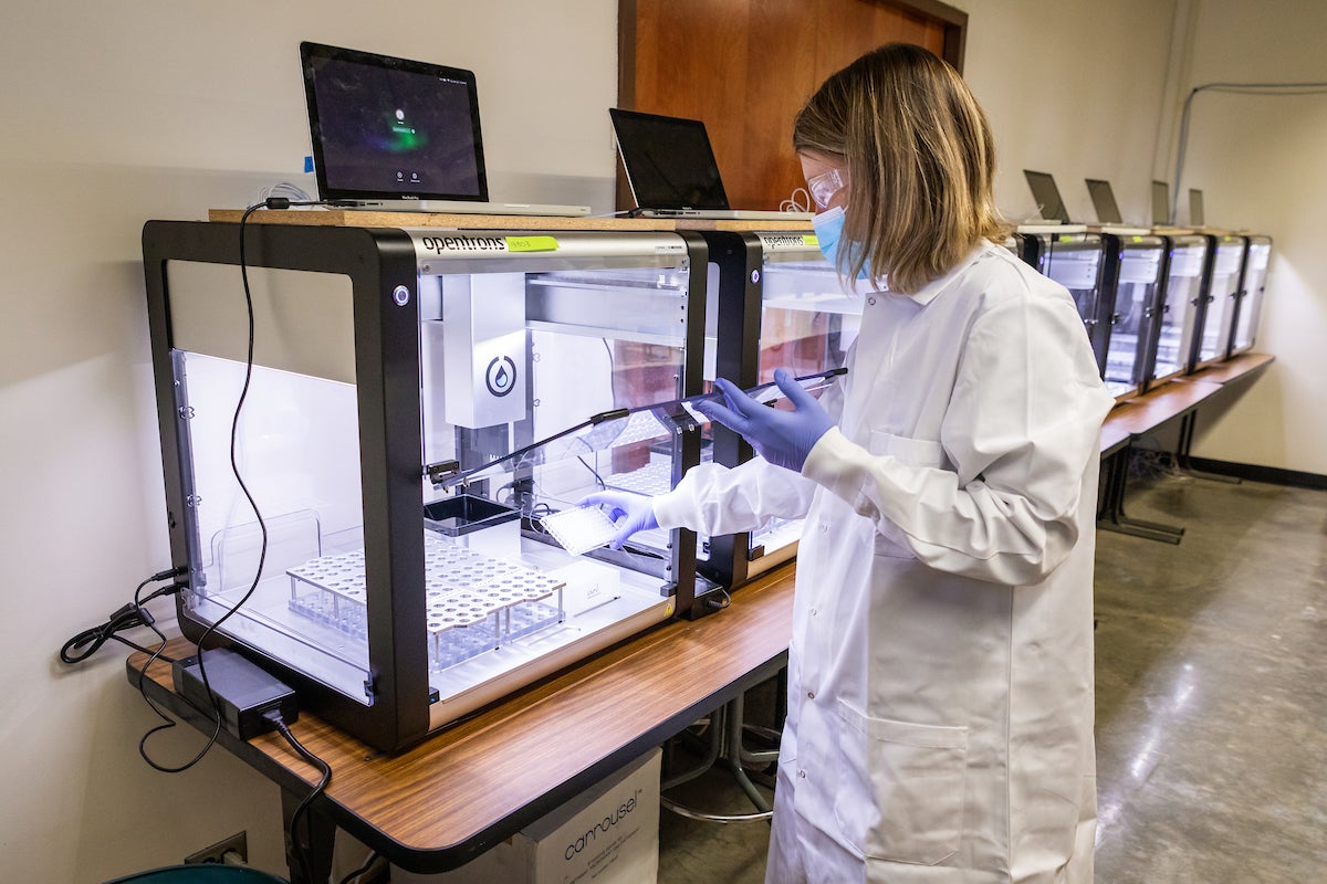 A woman in a lab coat, mask and gloves loads a tray of samples into a testing device