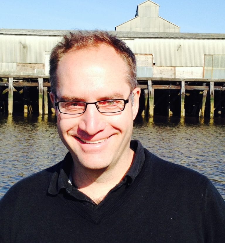 Professor Stefan Talke, smiling into the camera with an ocean jetty in the background