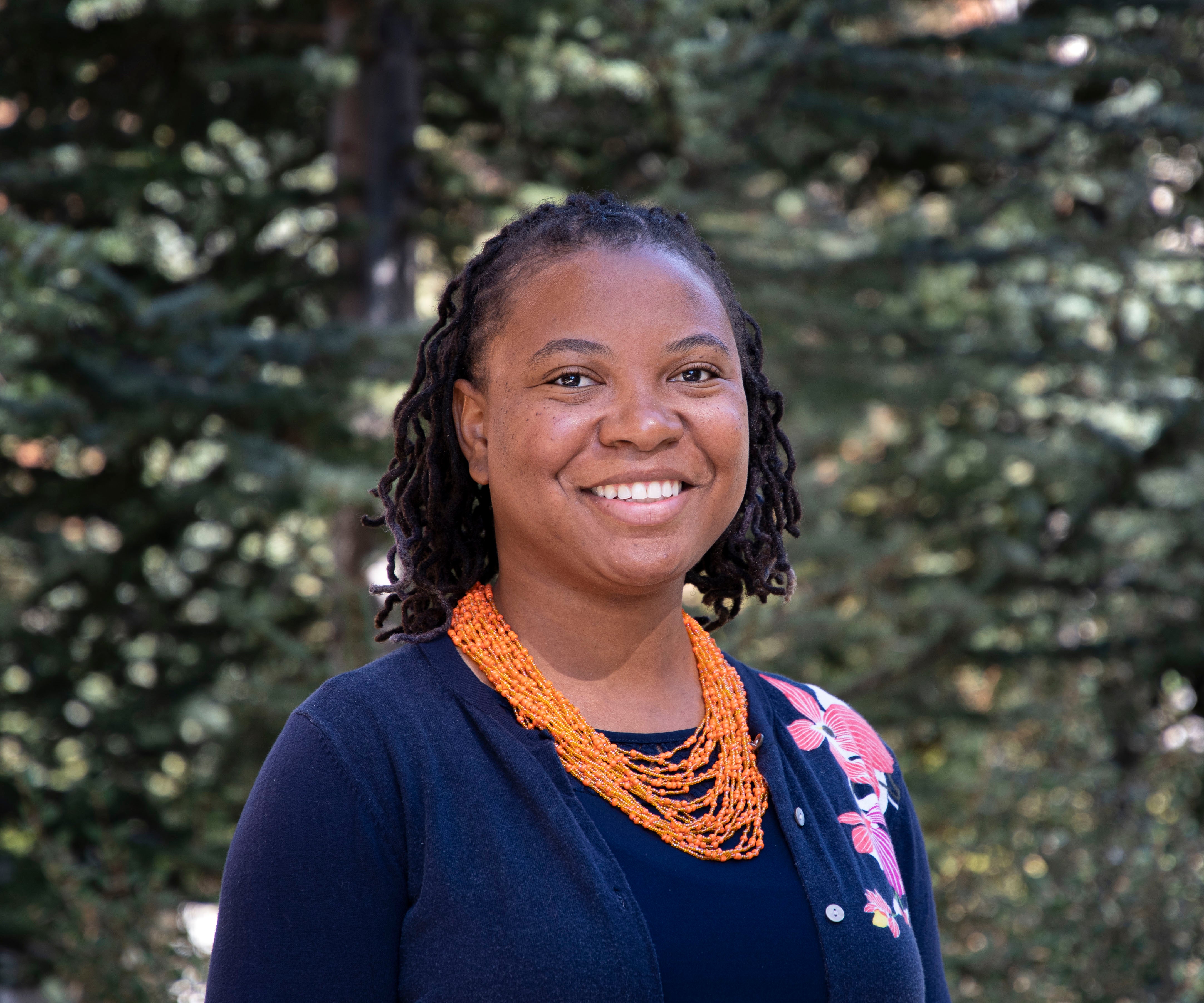 A headshot of professor Joni Roberts wearing a blouse and colorful orange necklace.