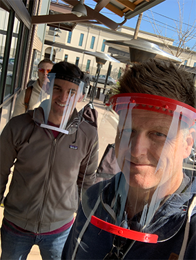 Three men wearing face shields stand in a line and pose for a photo.