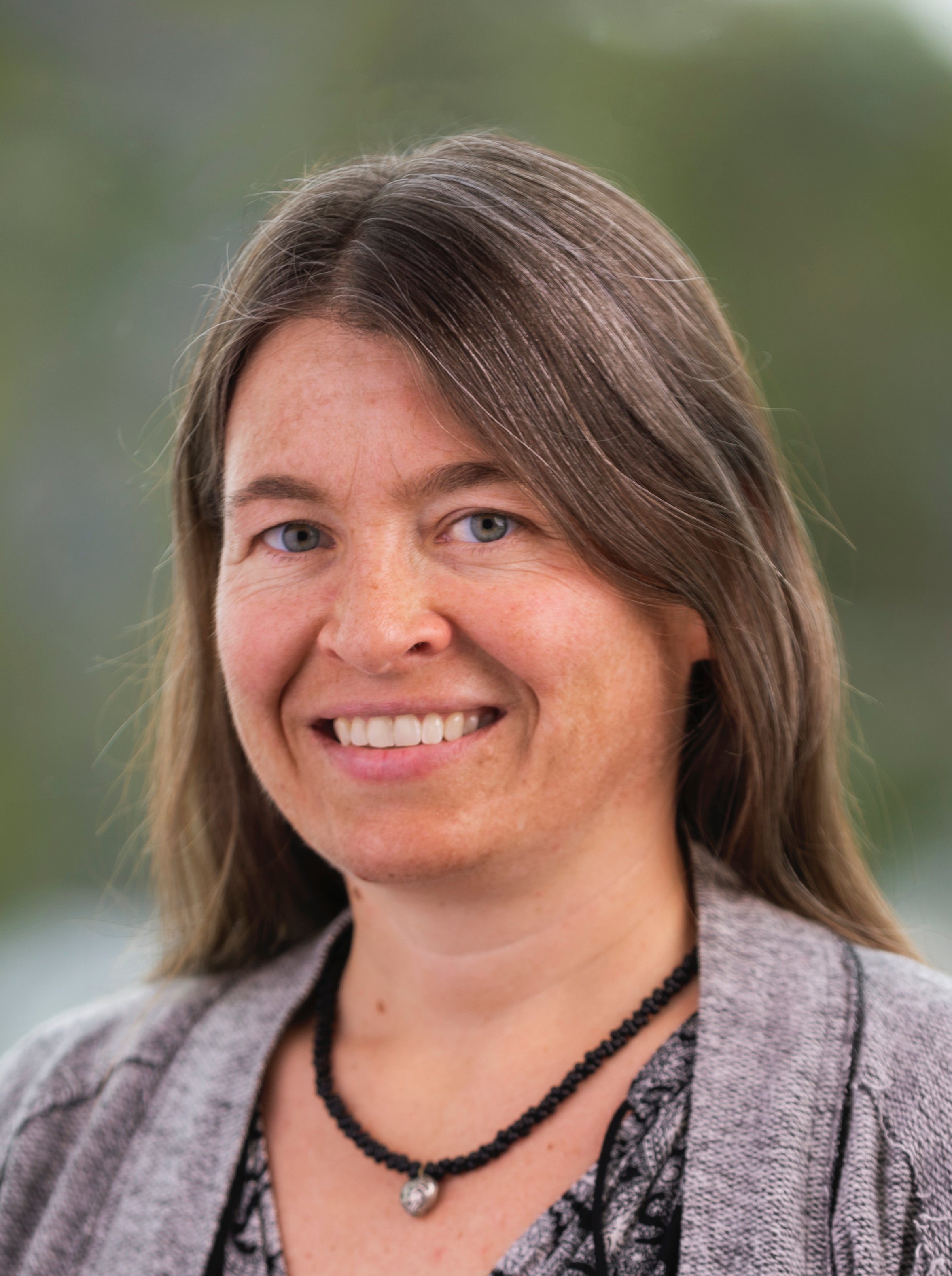 A woman wearing a cardigan smiles for a professional headshot.