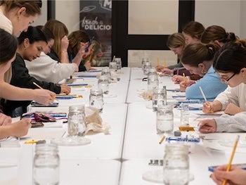 Students gather around a table and paint.