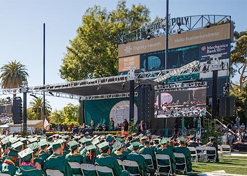 Seated graduates face the stage that includes a massive video screen at Spanos Stadium at a past comencement