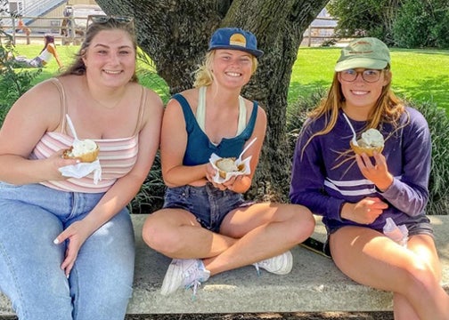 Three female students sit on a concrete bench each with a scoop of ice cream