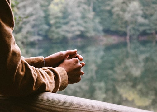 A person whose face is not seen leans arms on a railing in front of a scene of nature