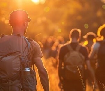 A group hikes through a field with backpacks on. 