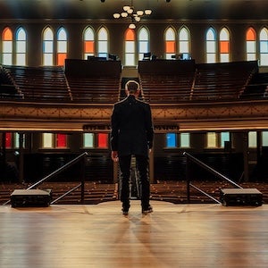 Randy Travis standing on stage facing an auditorium of empty seats.