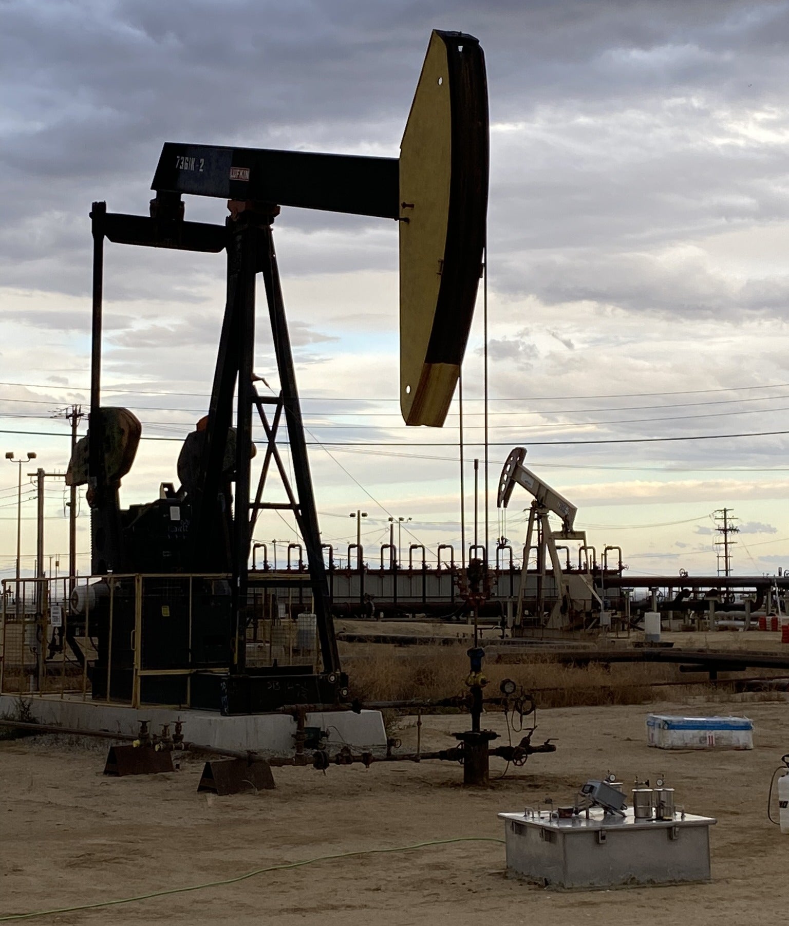 An abandoned oil derrick near several active ones.