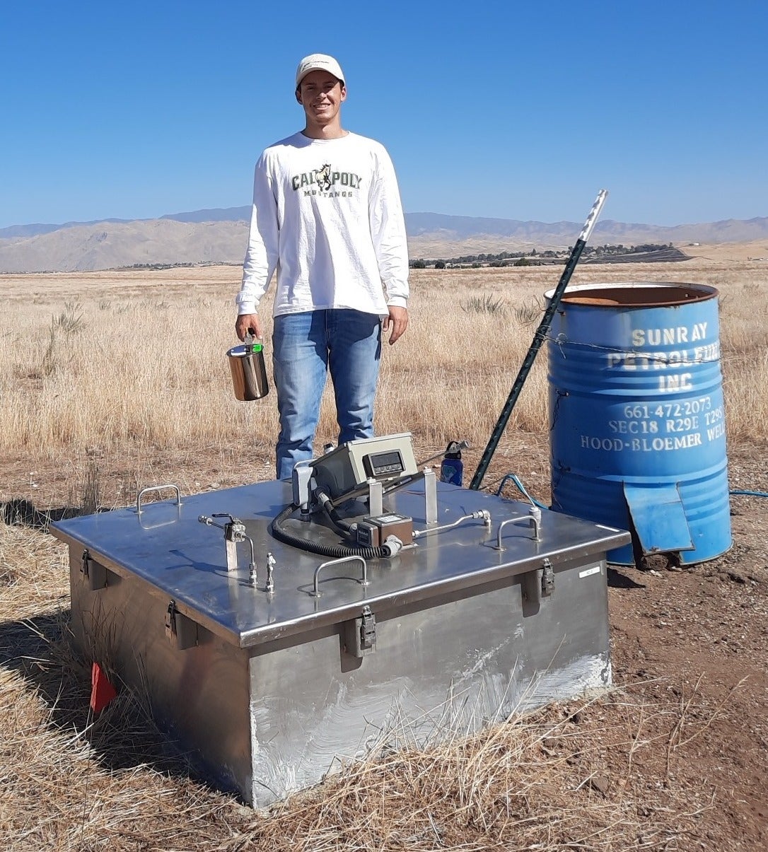 A student stands in a field next to a plugged oil well.