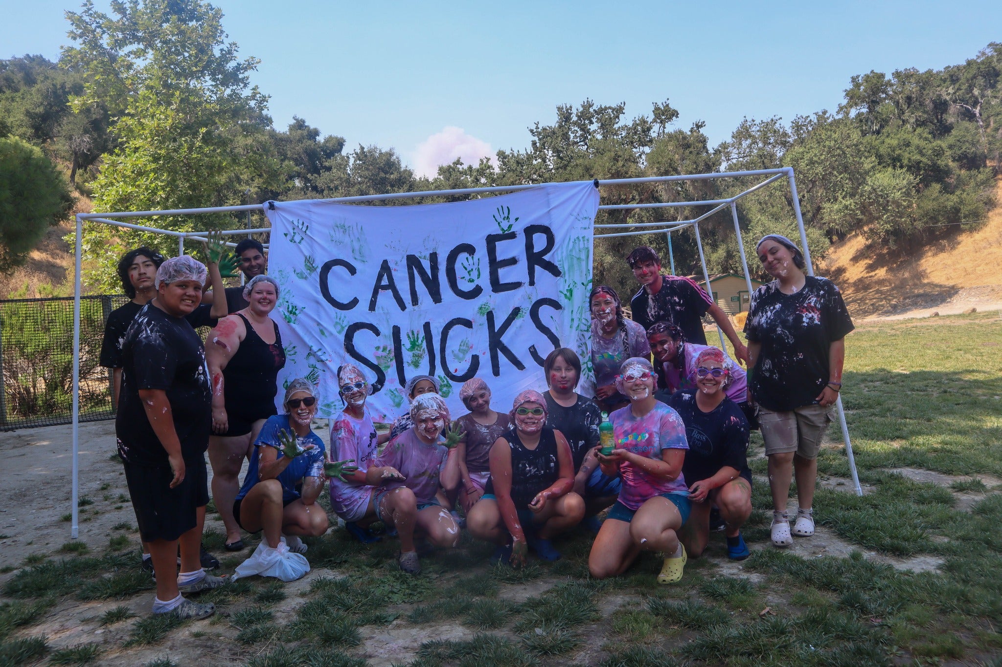 A group of smiling kids splattered with paint pose in front of a banner that reads "Cancer Sucks"