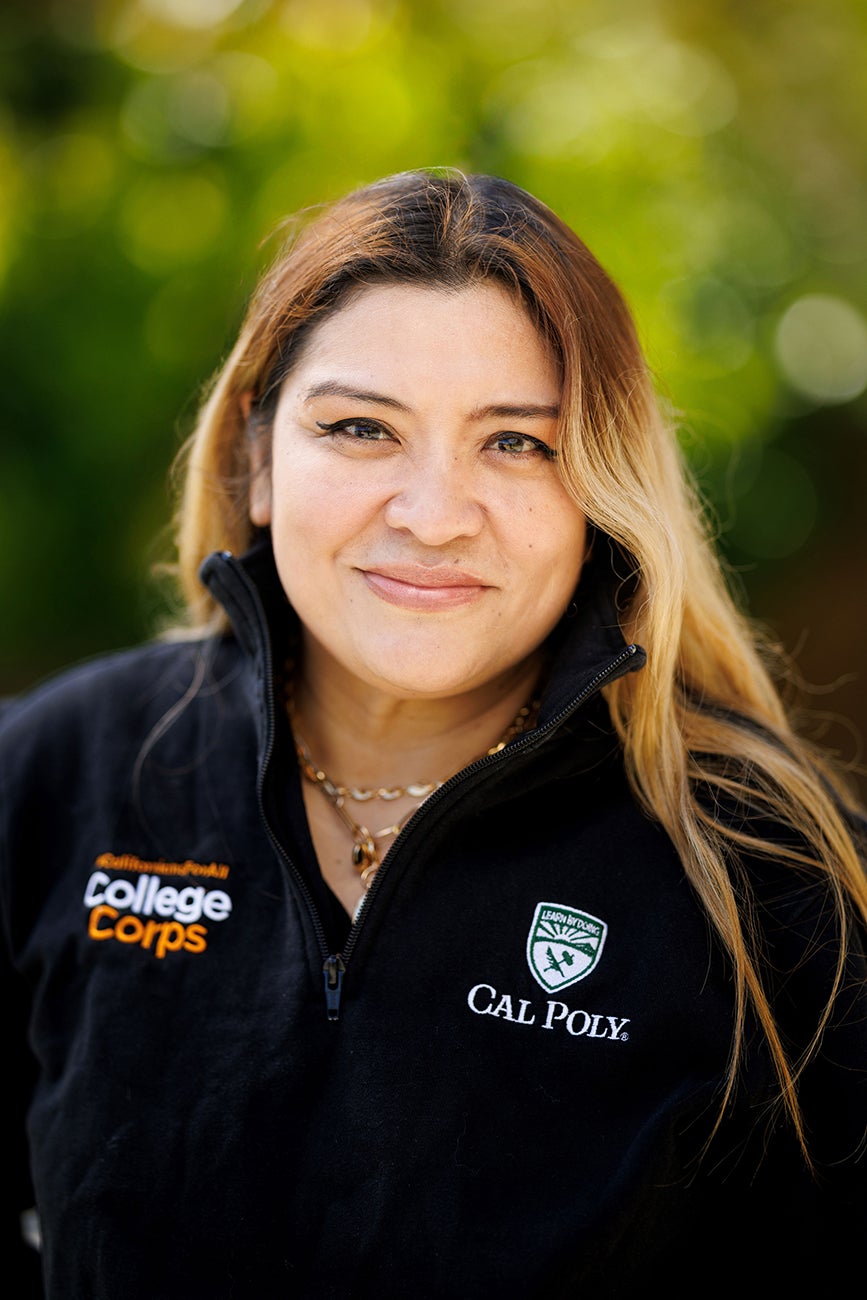 A woman in a black sweater with Cal Poly and College Corps logos smiles in a portrait.