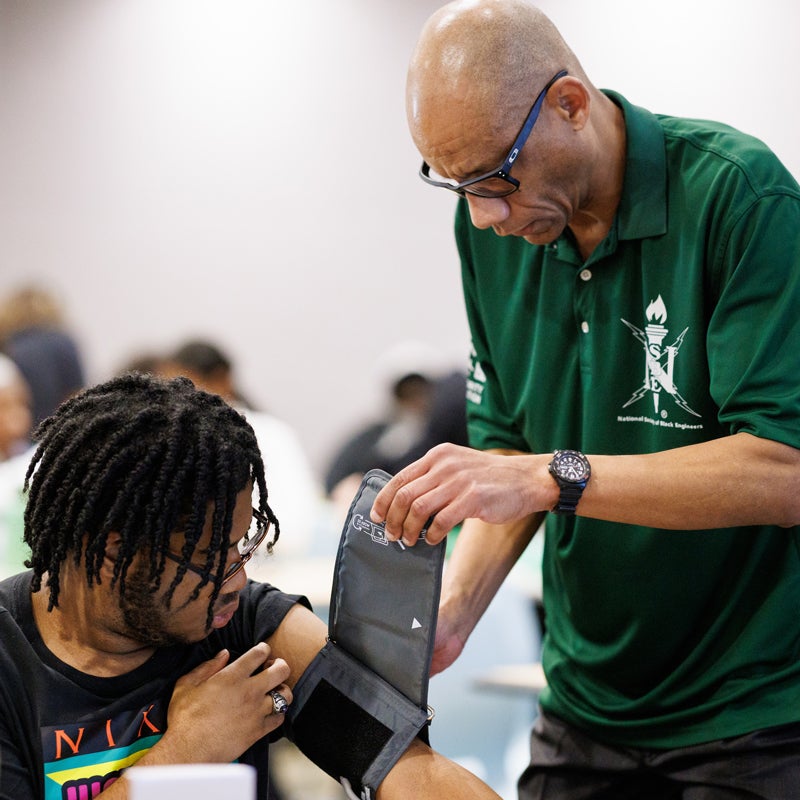 Professor Michael Whitt puts a blood pressure cuff on a student in a classroom