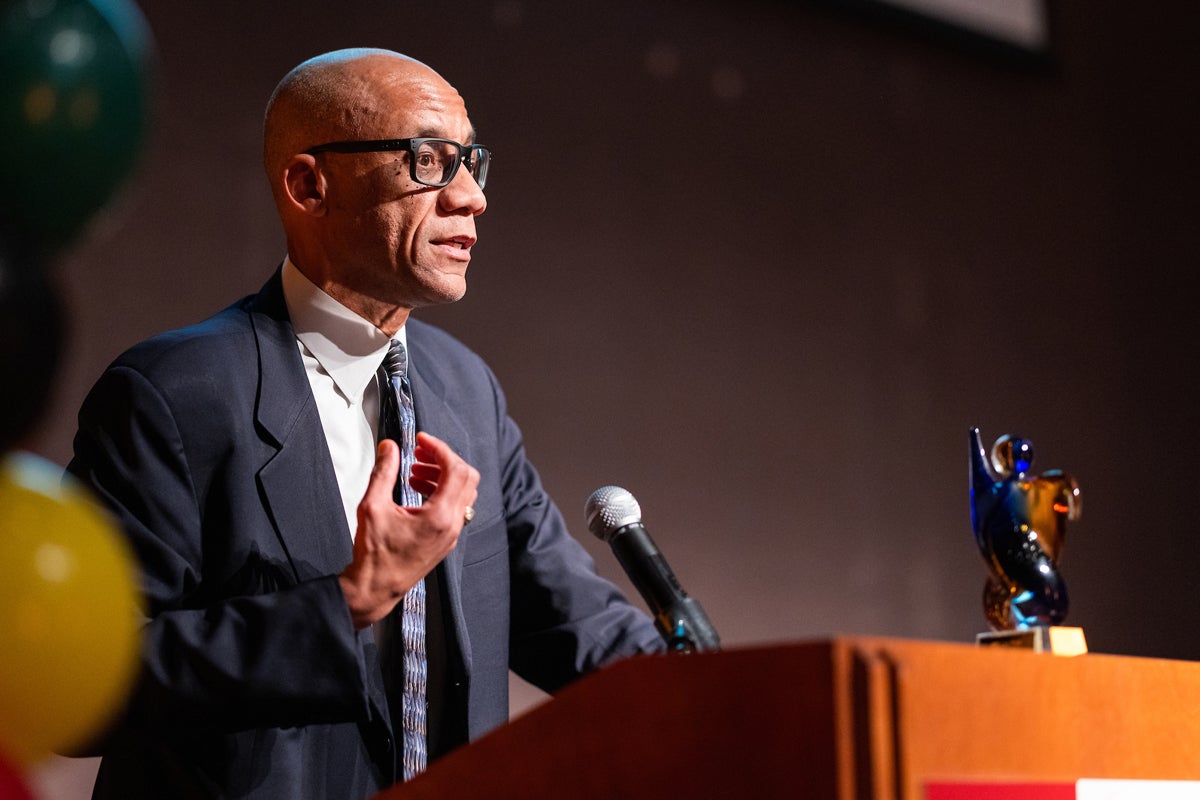 Professor Michael Whitt speaks at a podium with a blue glass statue