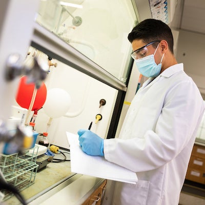 A lab assistant wearing a mask holds a clipboard and pen