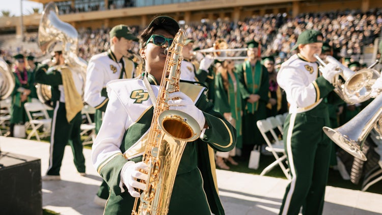 A saxaphone player and marching band members play in the middle of a commencement ceremony