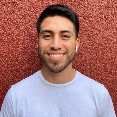 A man in a white shirt smiles standing in front of a red wall