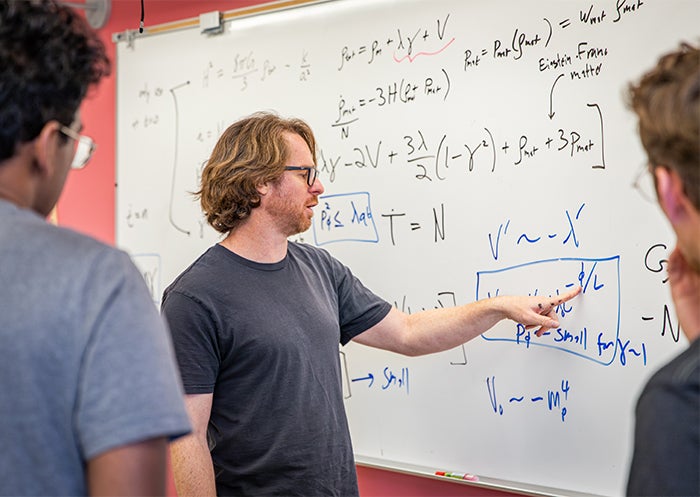 Physics professor Ben Shlaer points to a mathematical equation on a whiteboard.