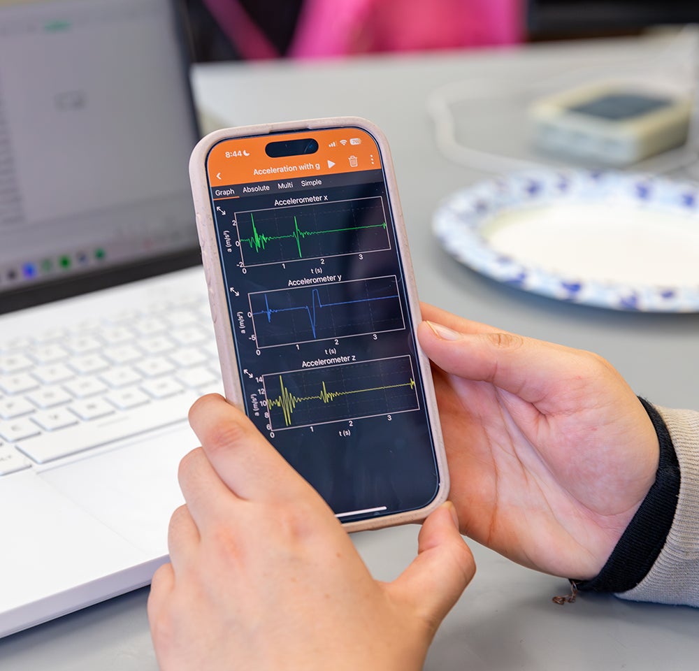 A student holds a phone with physics metrics on it. 