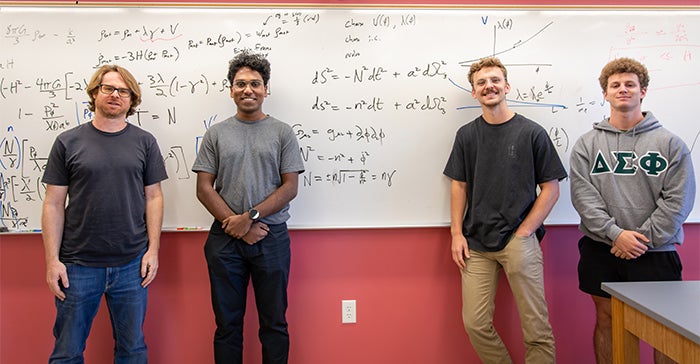 Professor Ben Shlaer and three of his students pose for a photo in front of a whiteboard full of their calculations.