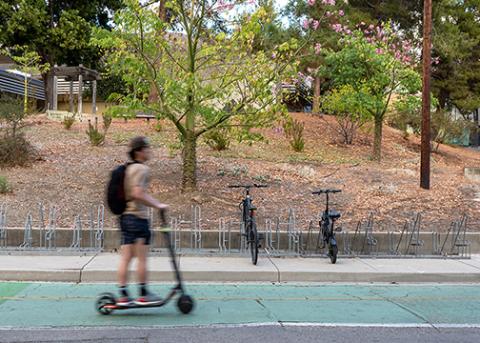 A male rider aboard a scooter travels on a campus roadway