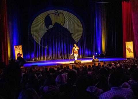 A darkened theater with a performer onstage giving a comedy show