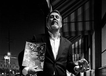 Author Victor Valle holds a booklet in his right hand and a bell pepper in his left in a black and white image