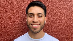 A man in a white shirt smiles standing in front of a red wall