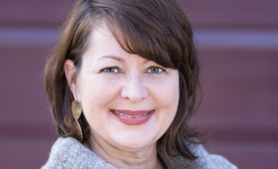 A woman with brown hair wearing a gray sweater smiles at the camera.