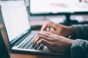 A close up of hands typing on a keyboard.