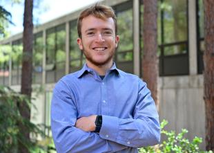 Tyler Coari wears a blue button down and smiles for the camera.