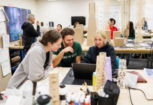 Architecture students work on a scale model of a skyscraper in a studio.