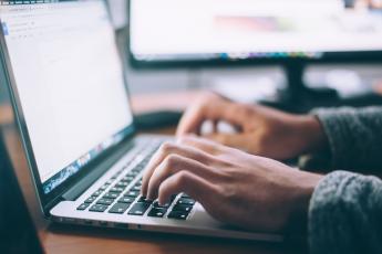 An unseen person types on a laptop keyboard.